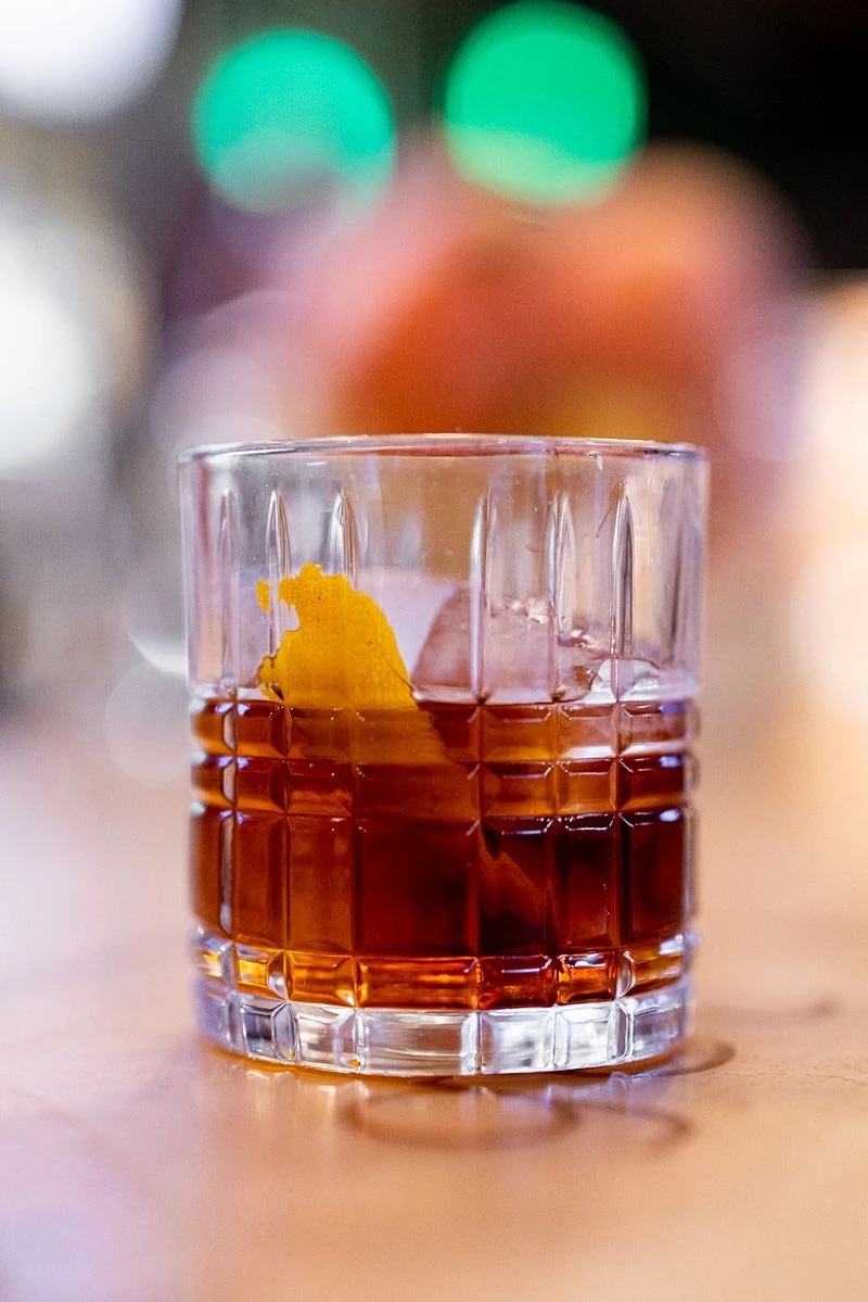 A Negroni over a single large ice cube with an orange peel, in a cut-glass rocks glass on a bar